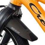 Oranssi lasten 16" jalkajarrullinen polkupyörä. Pyörässä on vakiovarusteina seisontatuki ja lokasuoja edessä. Lähikuva lokasuojasta.