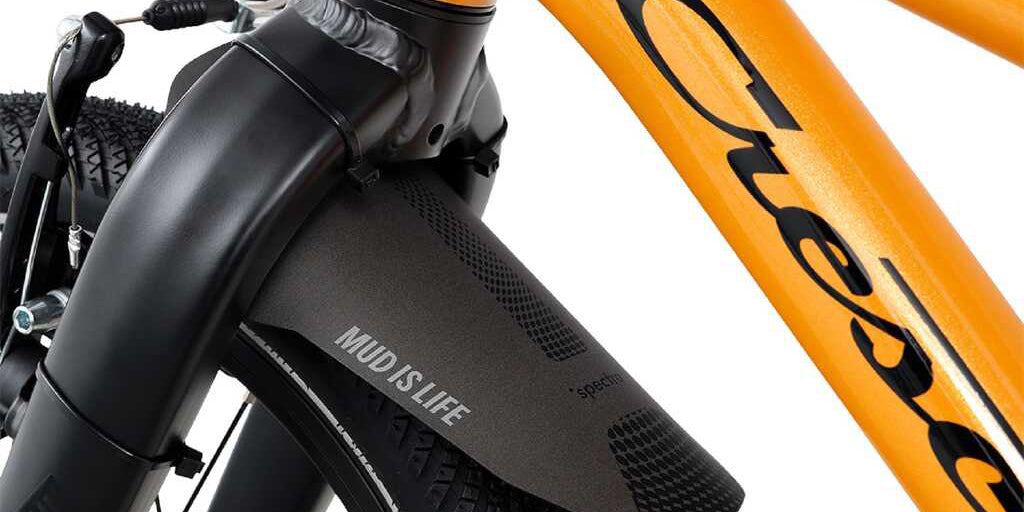 Oranssi lasten 16" jalkajarrullinen polkupyörä. Pyörässä on vakiovarusteina seisontatuki ja lokasuoja edessä. Lähikuva lokasuojasta.